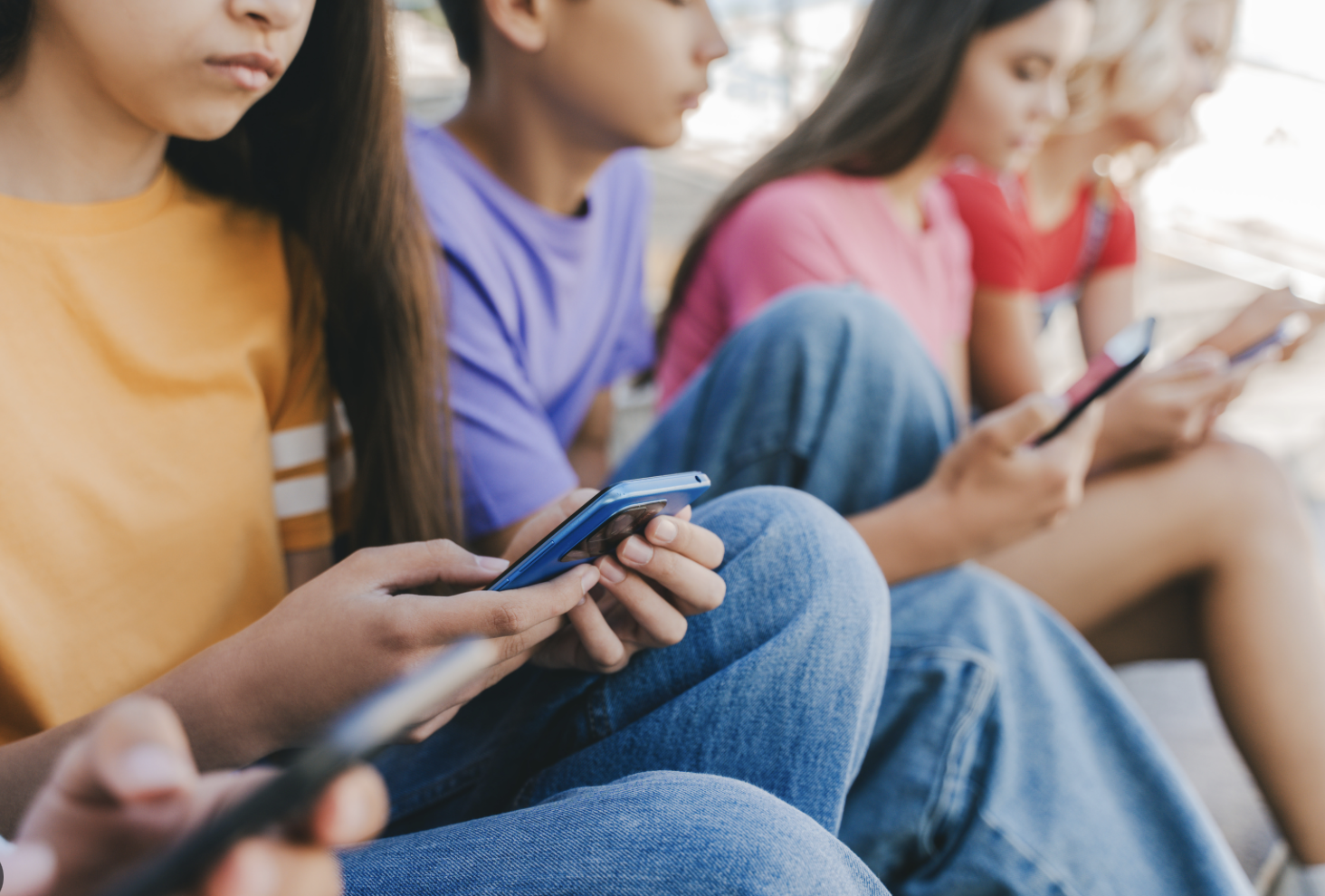 4 adolescents assis les uns à côté des autres avec un téléphone portable dans la main